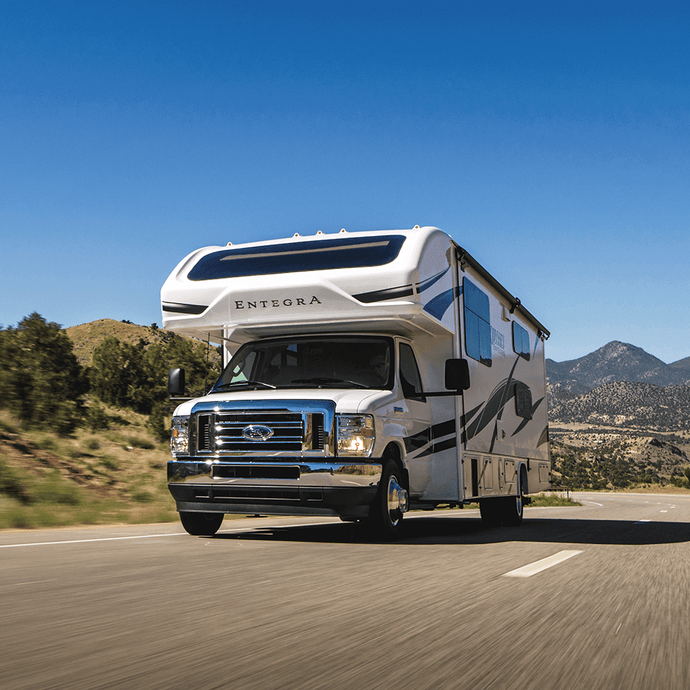 A Class C motorhome with its front tires visible, driving on a mountain highway