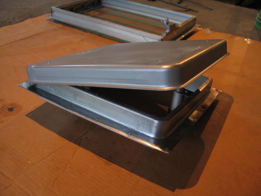 A removed RV roof vent housing sitting open on a workbench during a repair