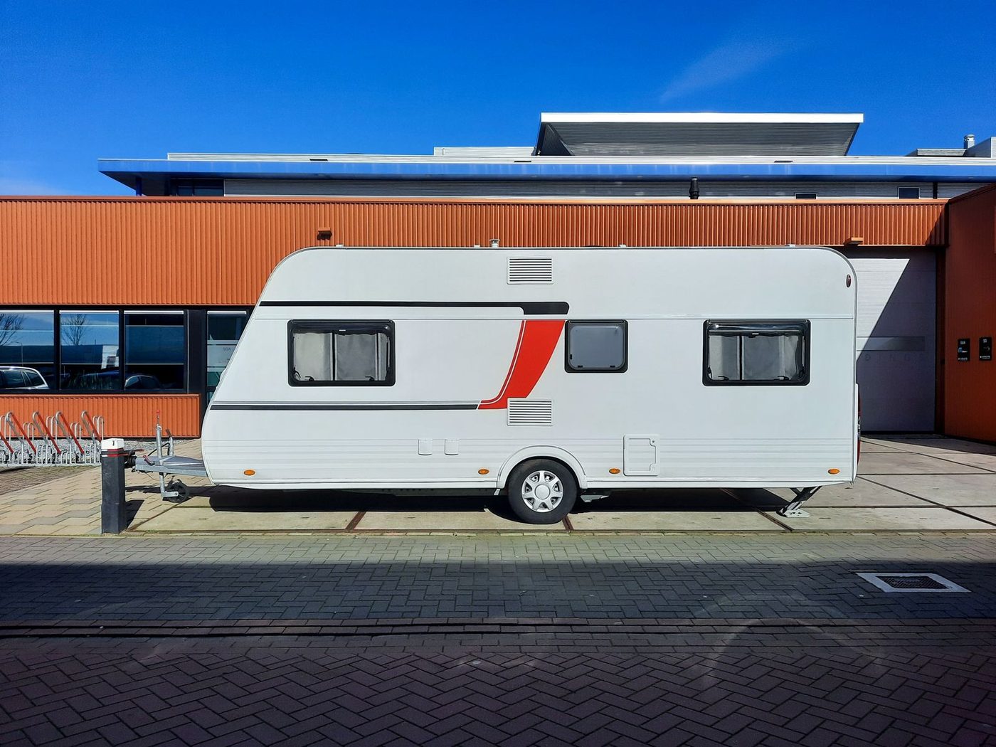 A sleek white caravan with red accents parked beside an industrial building