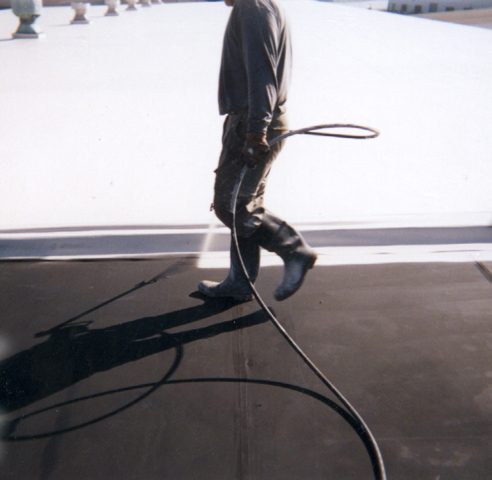 A roofing contractor applying an elastomeric roof coating to a flat roof with a paint roller