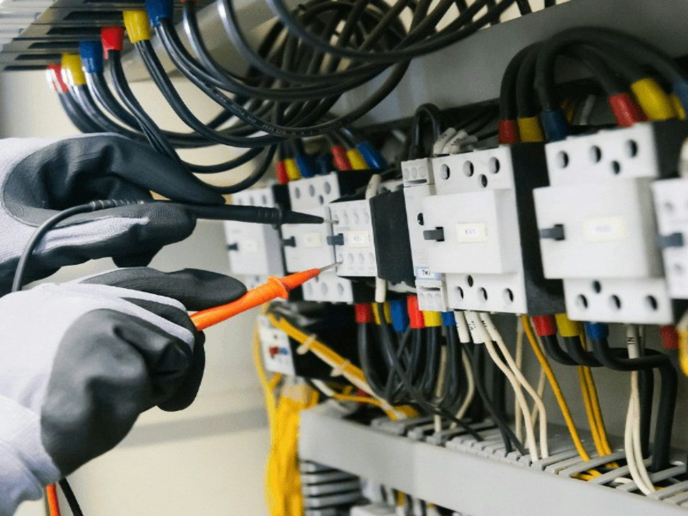 An electrician using a multimeter to test an electrical panel