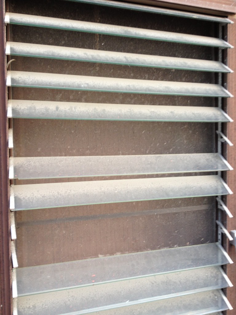Close-up of a jalousie-style window with stacked glass louvers and a hand crank