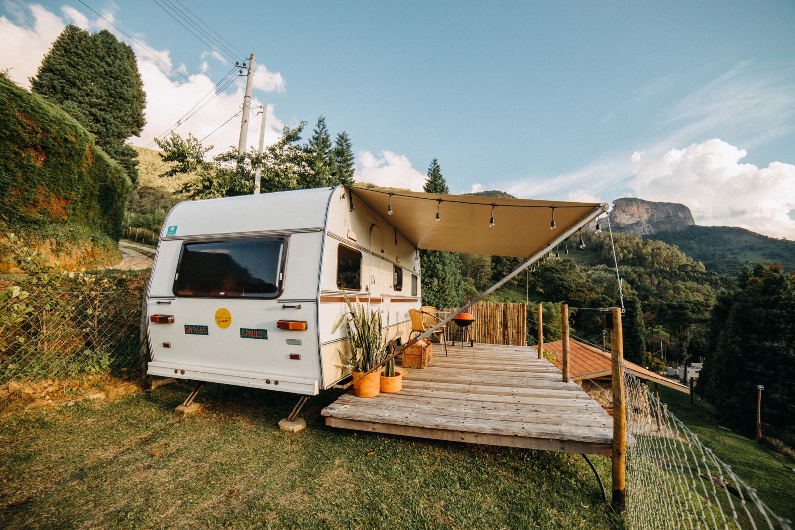 A camper trailer with its awning extended over a wooden deck at a mountain campsite