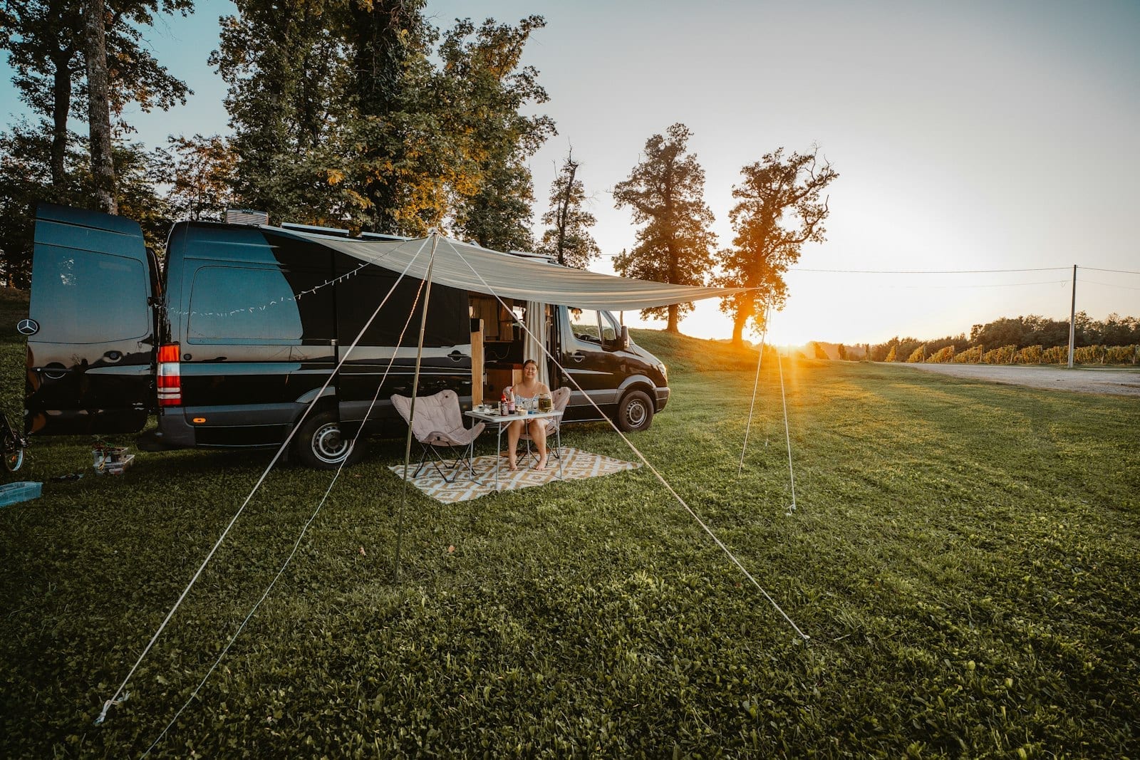 A couple relaxing in camp chairs under a camper van awning at sunset