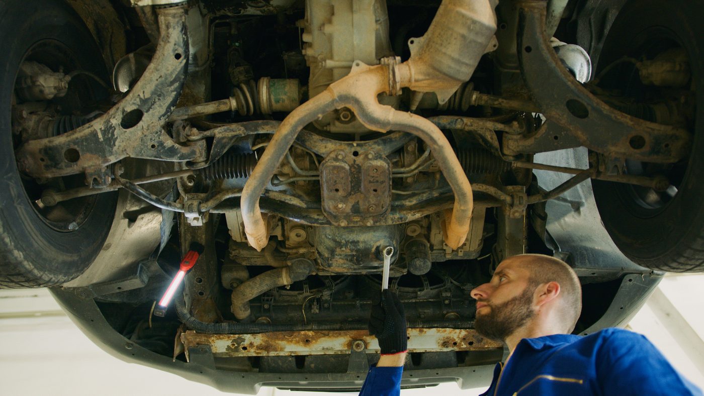 A mechanic examining the underside of a vehicle in a garage