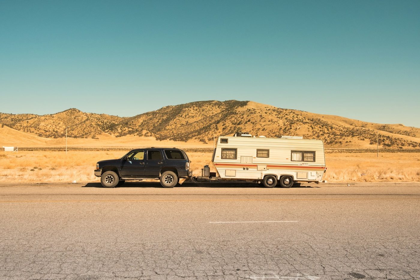 A black SUV towing a white trailer along an open highway