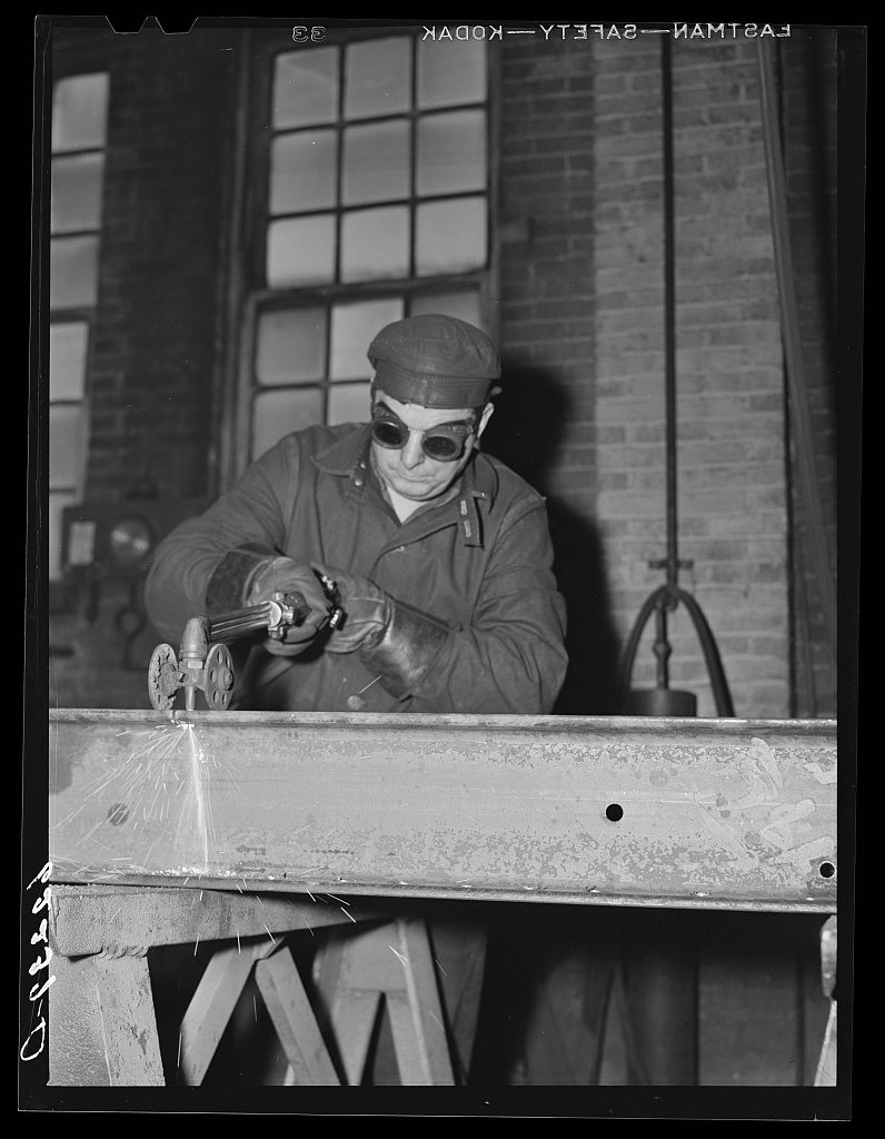 A structural steel shop worker using an acetylene torch to cut metal, sparks visible
