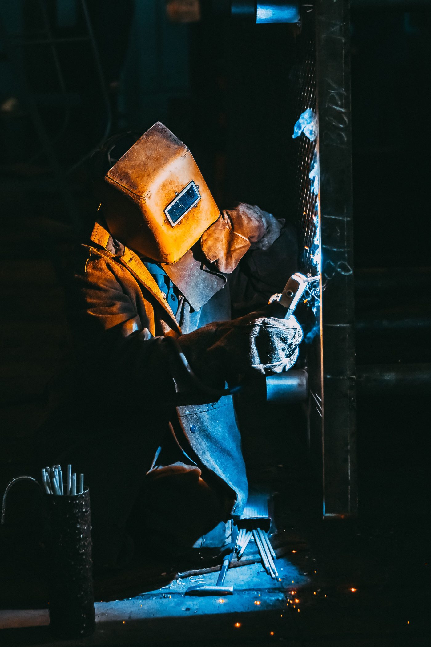 A welder in safety gear working on metal, sparks flying in a dimly lit industrial workshop