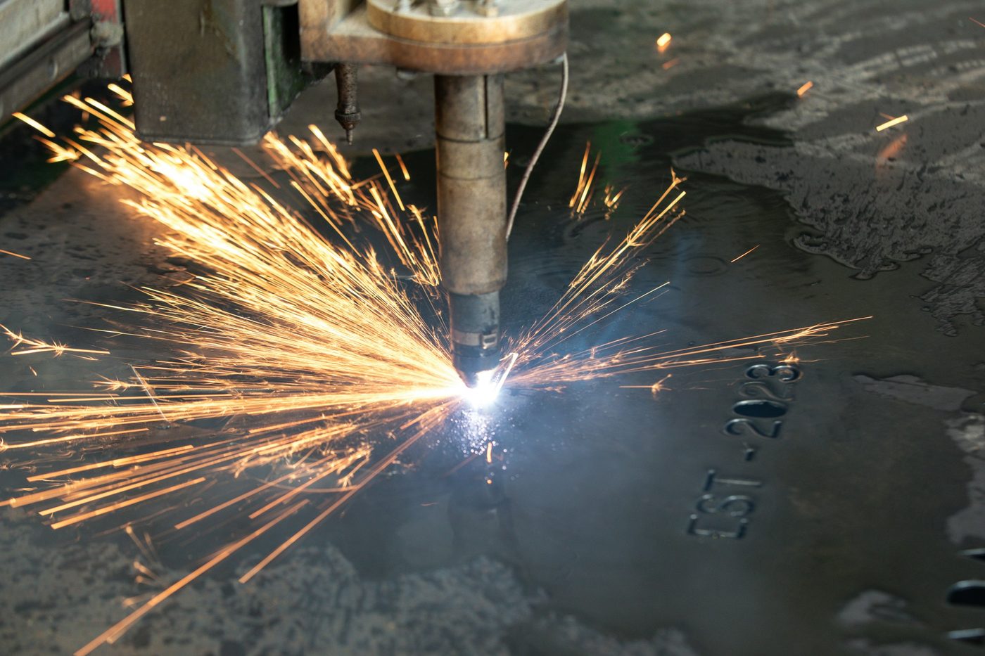 A welder using an acetylene torch to cut a piece of steel, orange sparks visible against a dark background