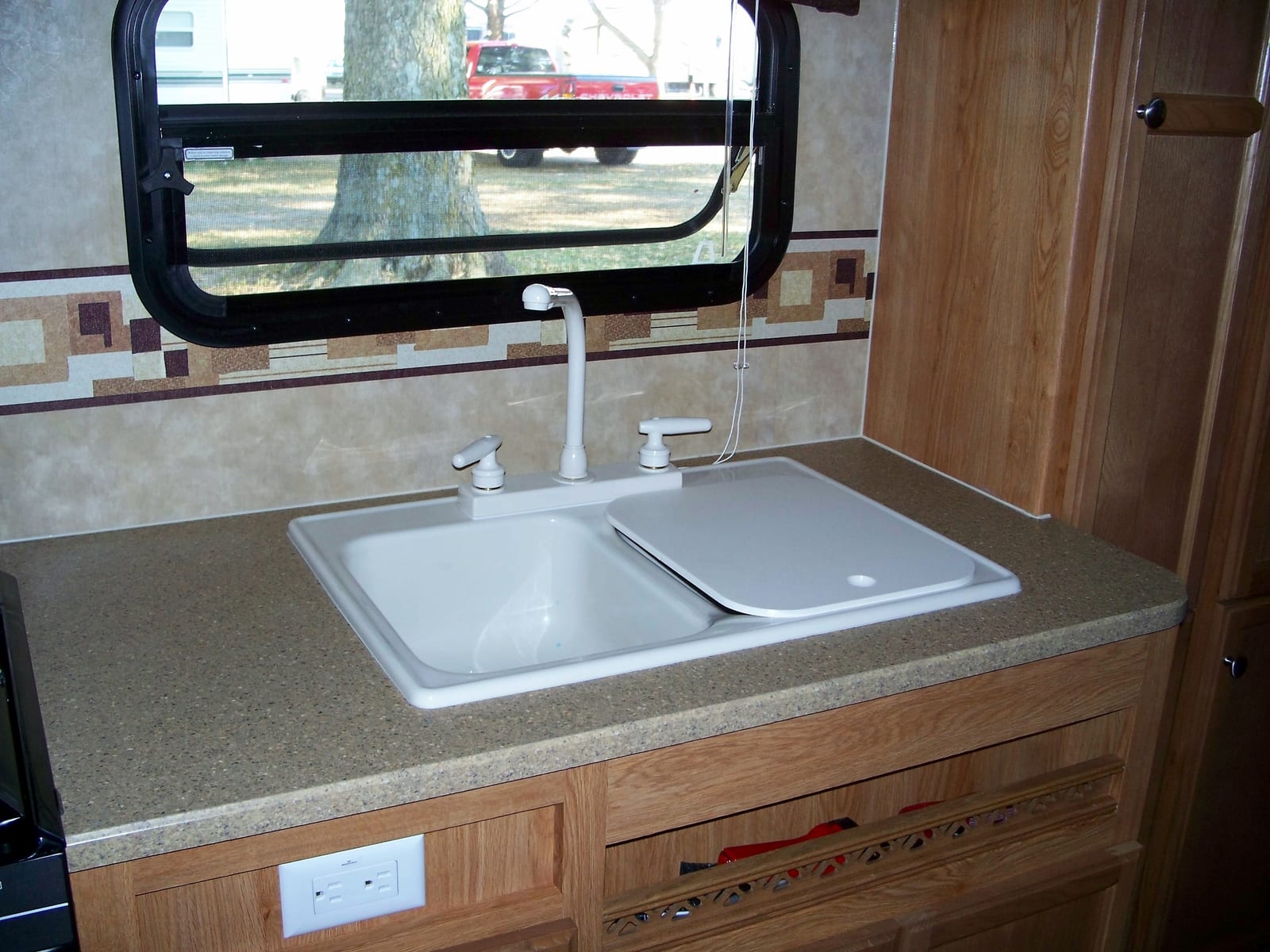 RV kitchen sink and faucet beneath an open screened window
