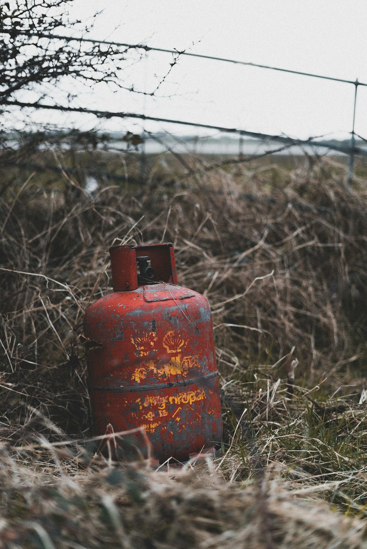 A single portable red propane cylinder sitting alone on grass