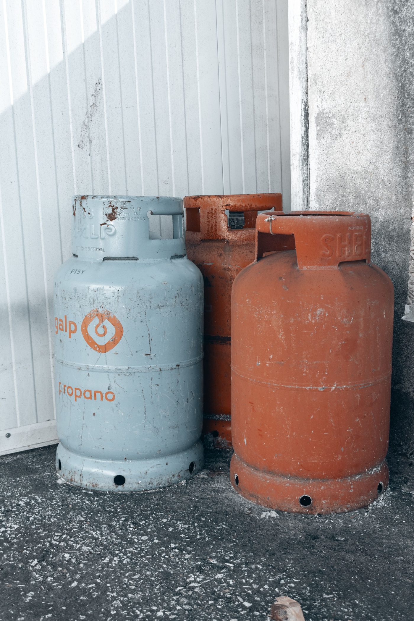 Three propane gas tanks of varying condition standing against a concrete wall