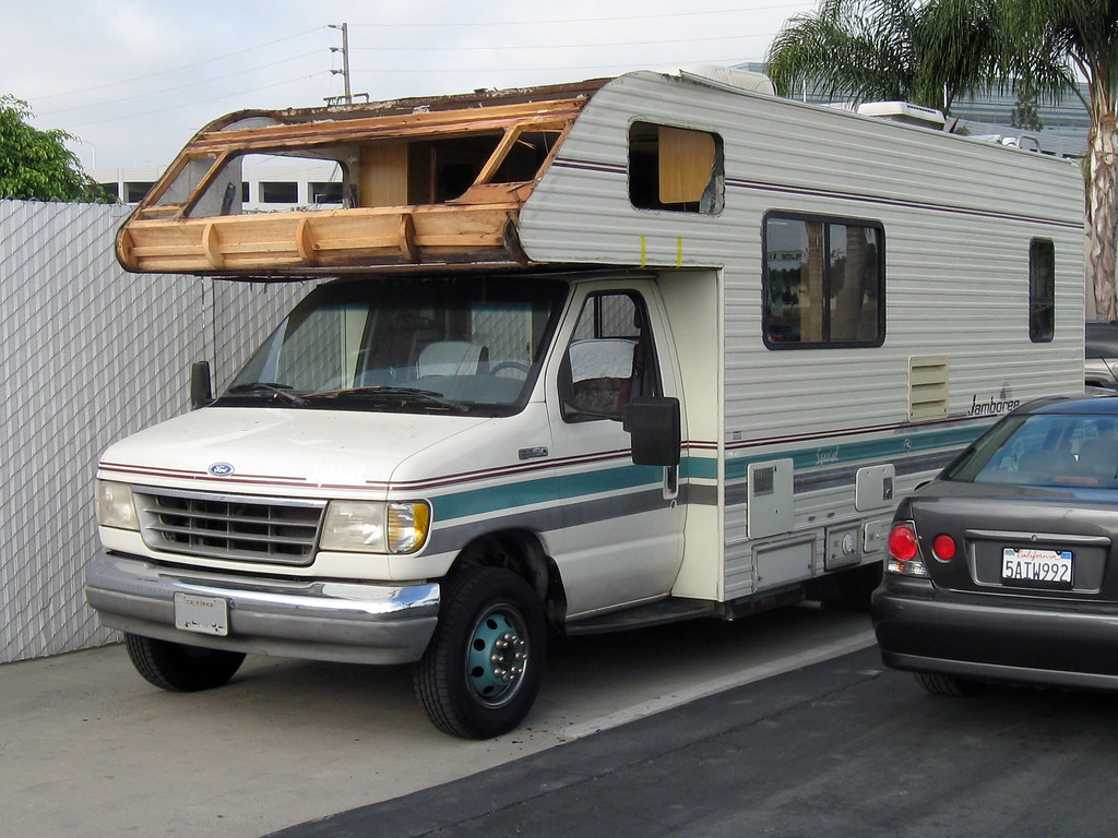 A Class C motorhome with its cabover roof rotted and peeled open from long-term water intrusion