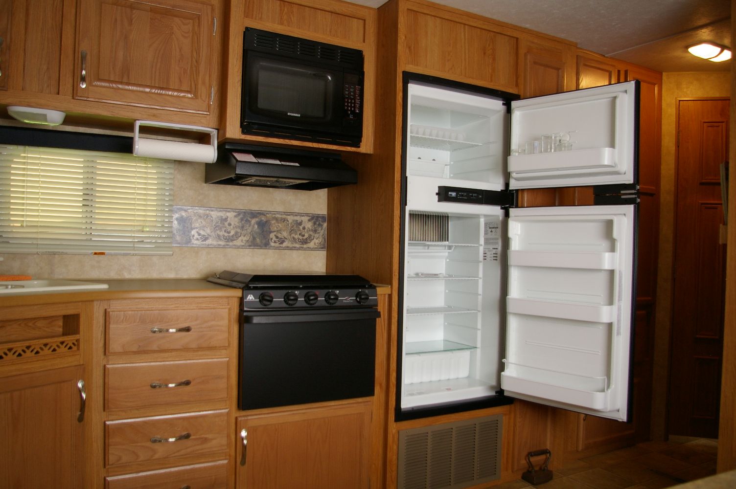 RV kitchen slide-out with refrigerator door open showing shelving