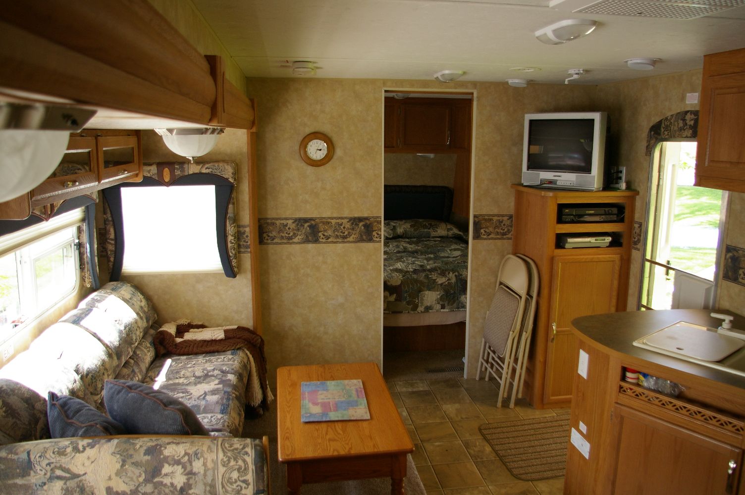 RV living room slide-out with sofa, TV stand, and bedroom view