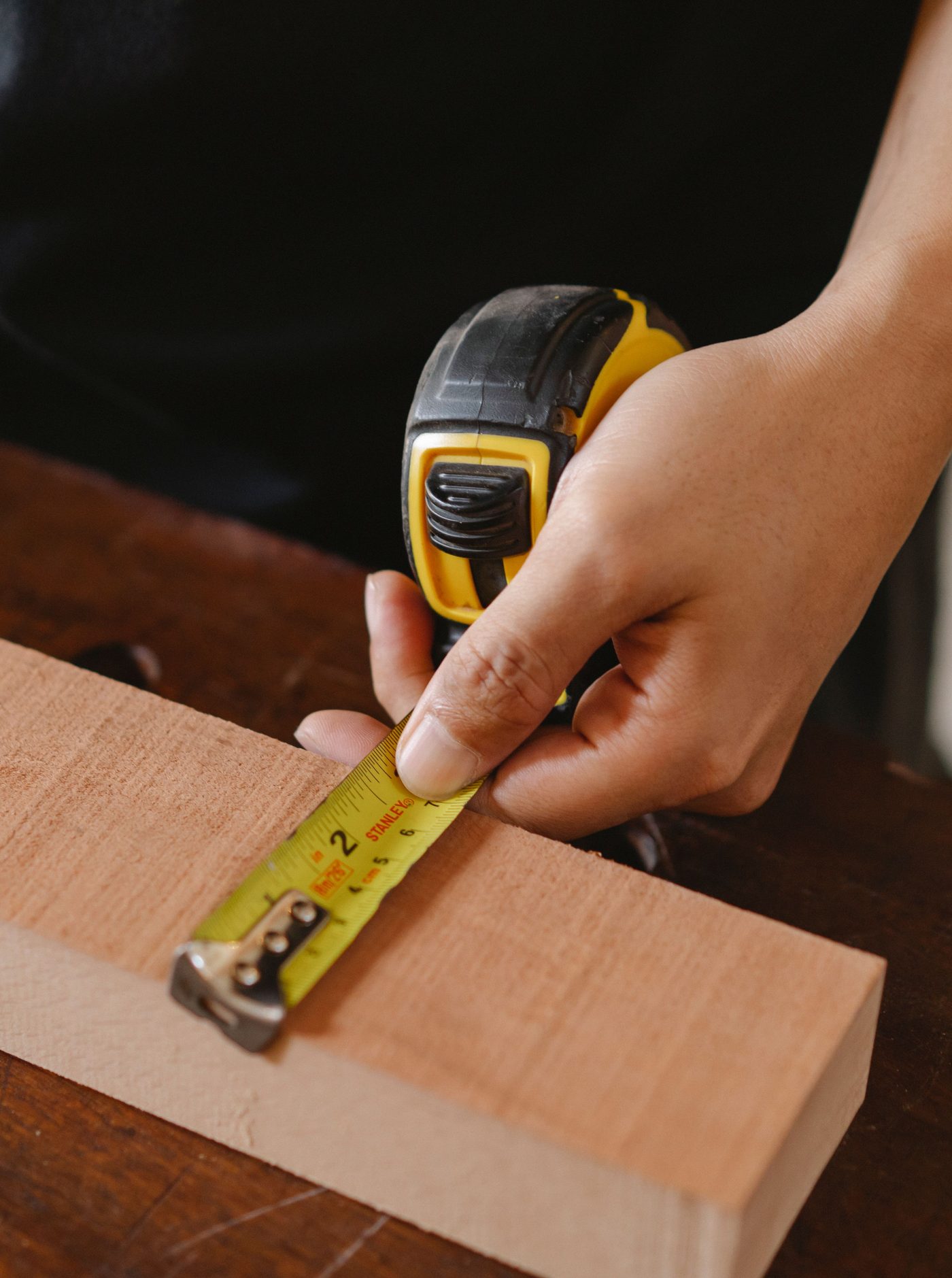 A close-up of hands using a tape measure to measure a wood plank in a workshop
