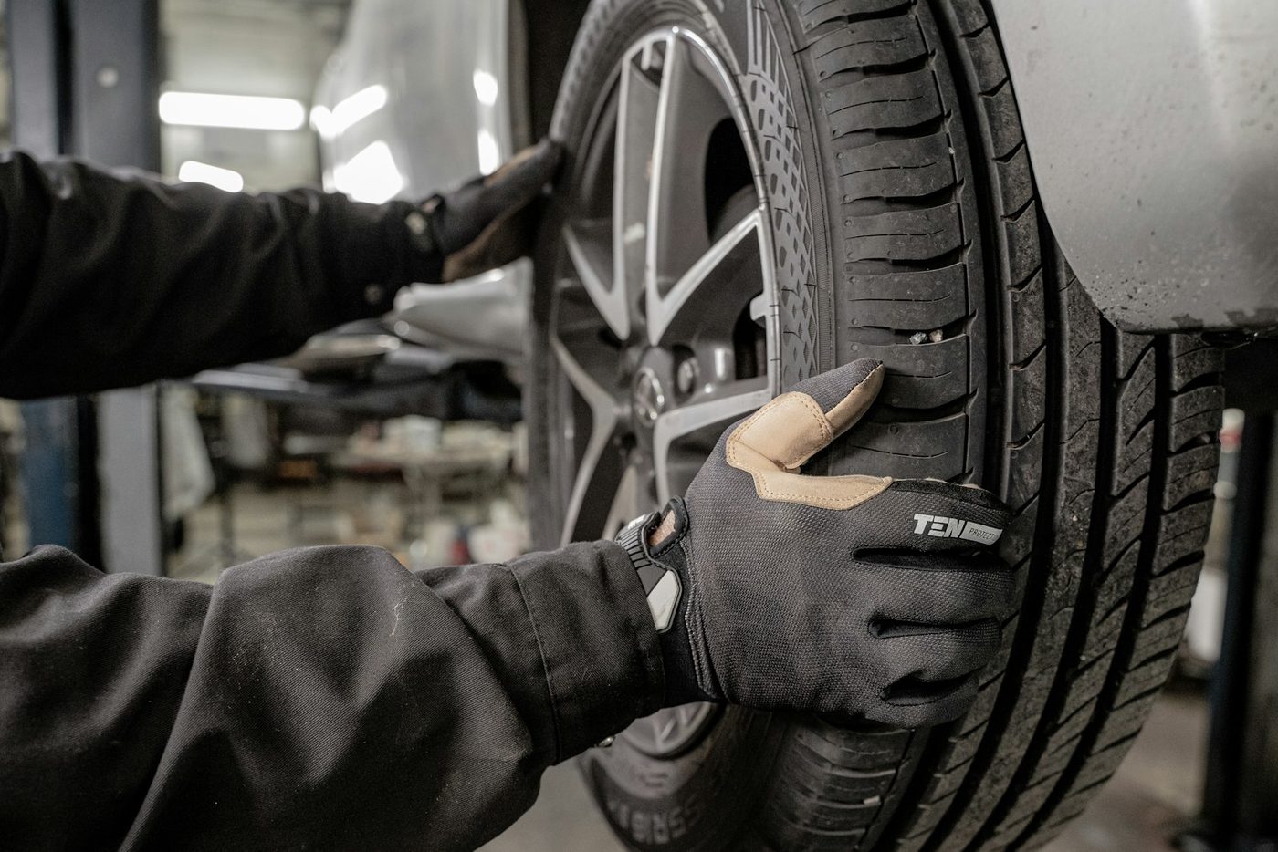 A mechanic wearing work gloves inspecting a tire mounted on a vehicle in a shop