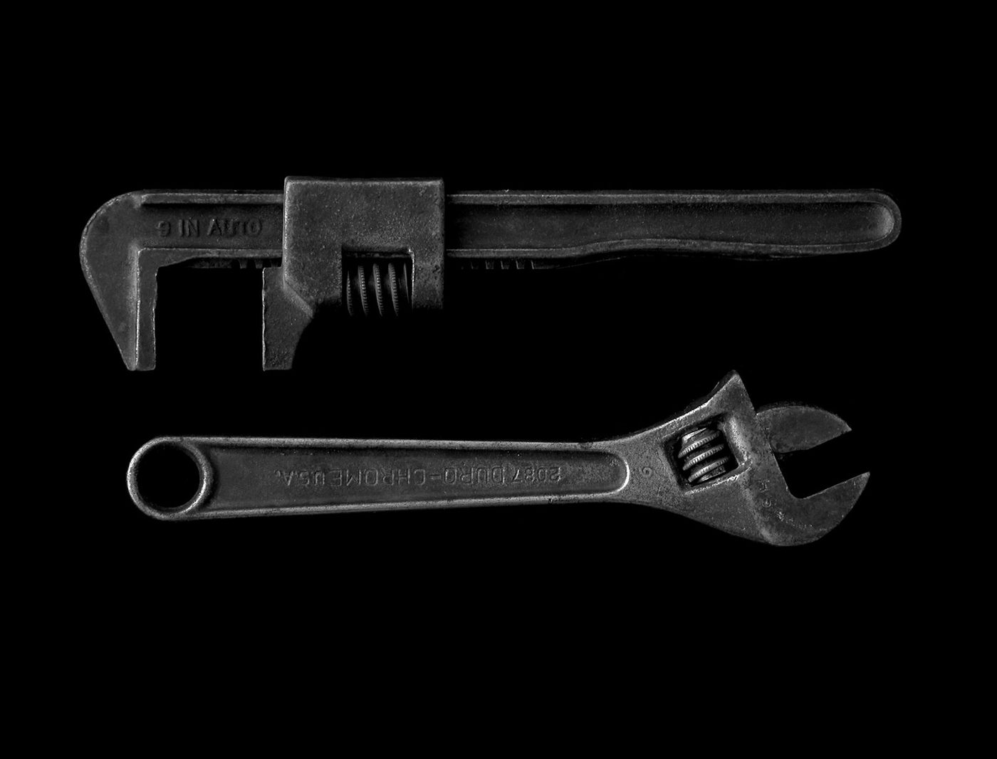 A gray adjustable wrench and pipe wrench laid out for a plumbing repair