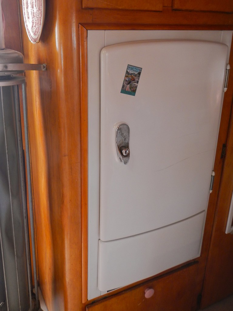 Vintage camper refrigerator with a rounded white door in a wood cabinet