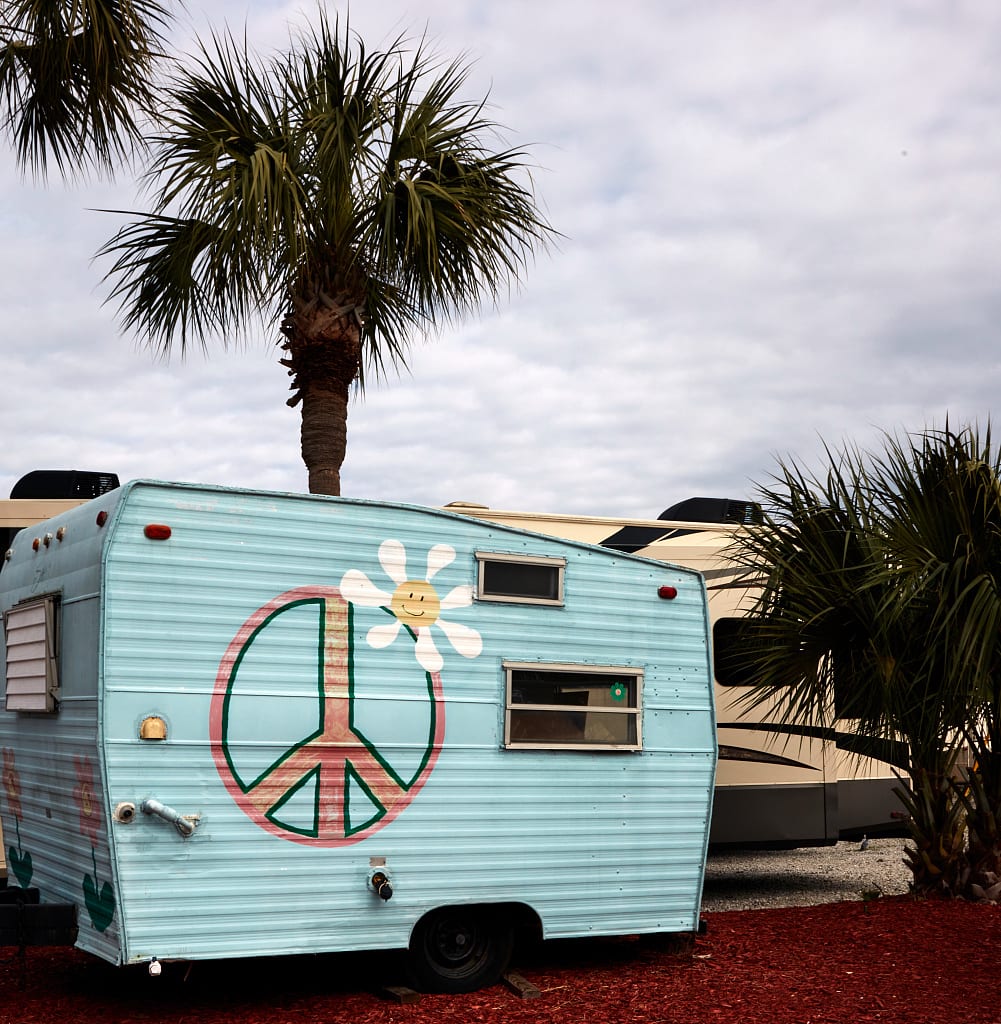 A small vintage-style travel trailer parked at an RV dealership, resting on its axle and wheels