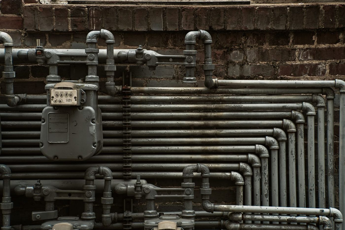 A detailed view of industrial steel pipes and a gas meter on a brick wall
