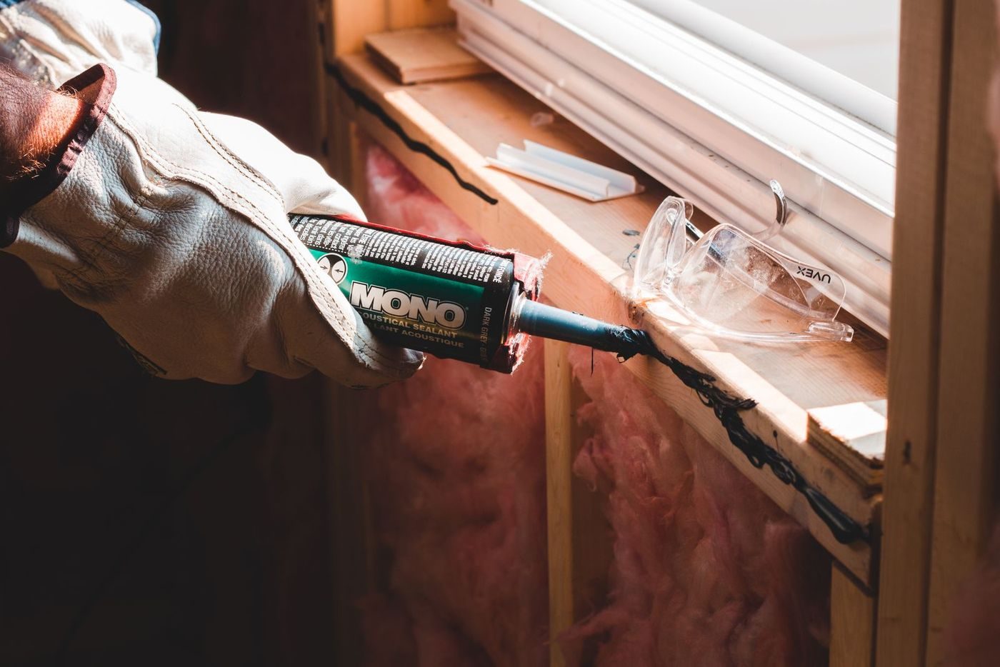 A worker applying a bead of sealant along a window seam with a caulk gun