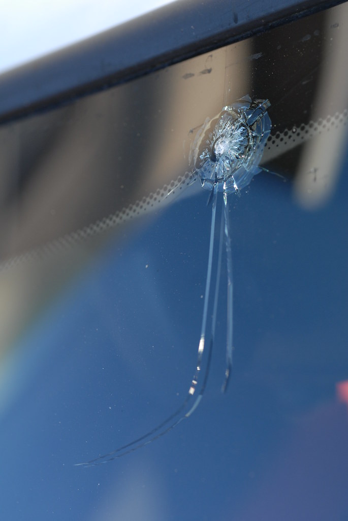 Bullseye rock-chip impact on a windshield with cracks trailing toward the wiper blade