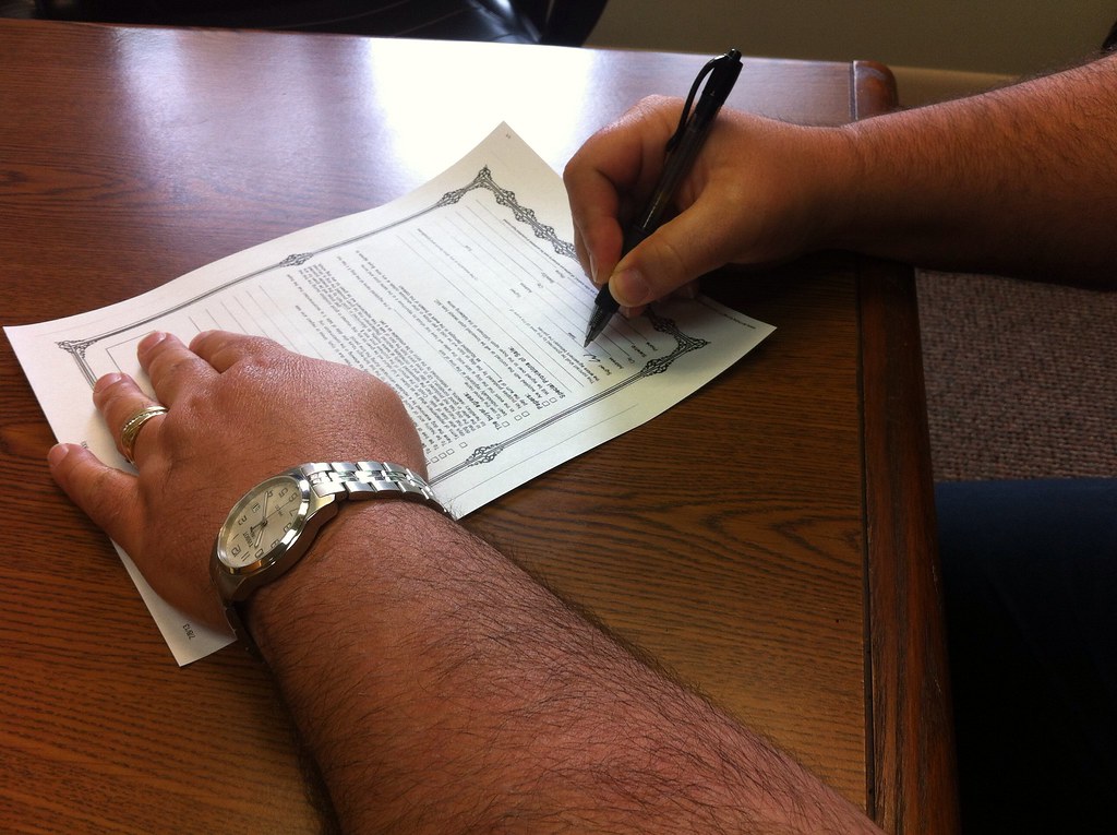 Close-up of hands signing a formal paper contract on a wooden desk